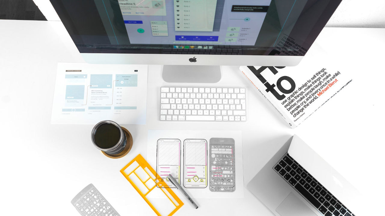 The top view of Apple iMac, sketches of mobile application on the paper, cup of coffee on white table