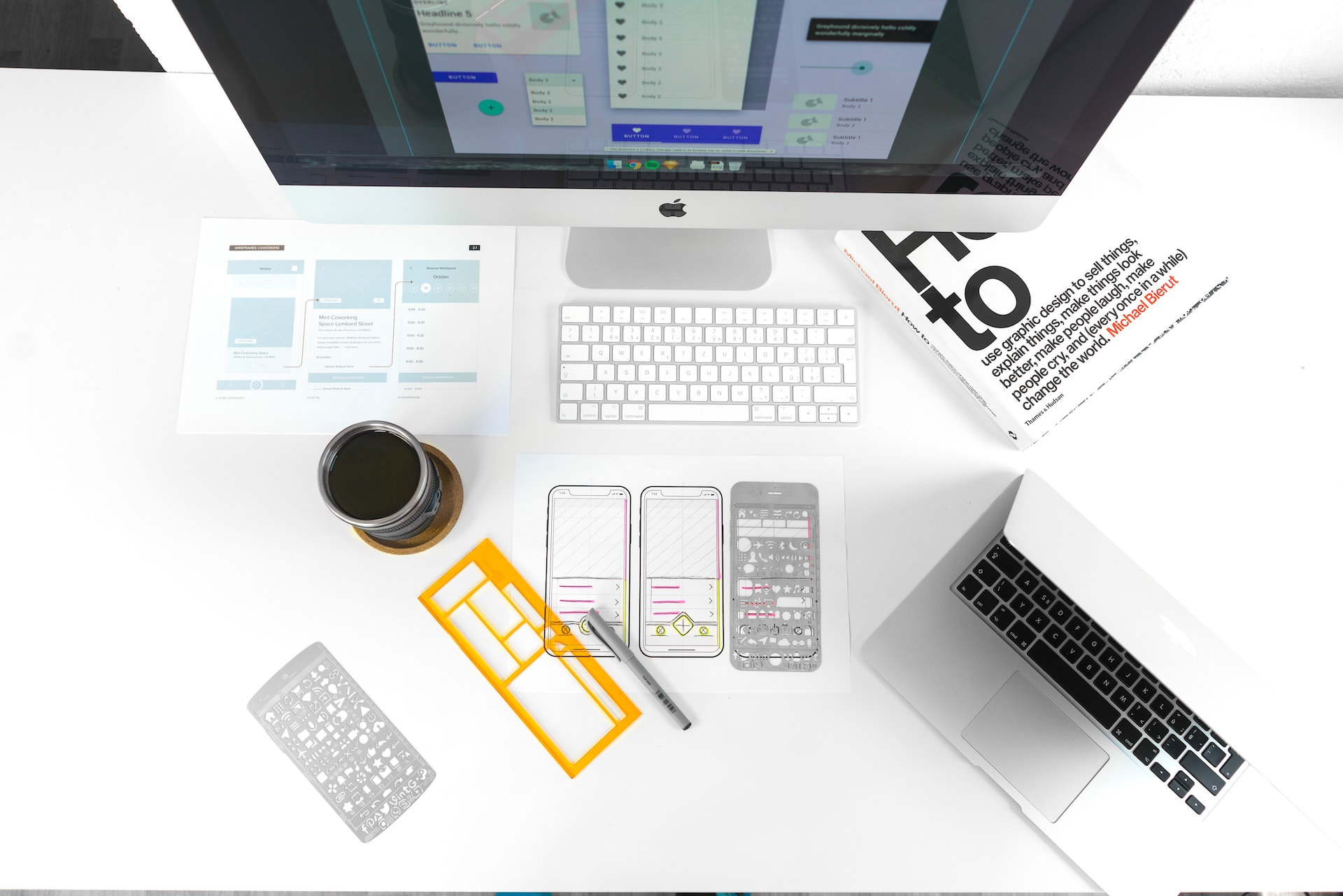 The top view of Apple iMac, sketches of mobile application on the paper, cup of coffee on white table